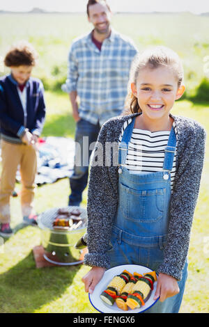 Portrait of smiling girl avec des brochettes de légumes ensoleillés au camping Banque D'Images