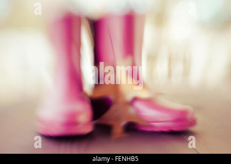 Une paire de bottes de pluie rose avec un effet de flou, de s'asseoir avec une grande feuille de chêne en automne Banque D'Images