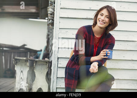 Portrait of smiling brunette woman drinking coffee on porch Banque D'Images