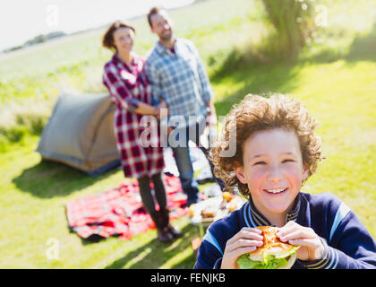 Portrait of smiling boy eating hamburger avec les parents de camping Banque D'Images