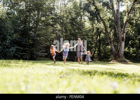 Mid adult woman et trois jeunes filles se tenant la main et running in park Banque D'Images