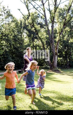 Mid adult woman running et tenir la main avec trois filles dans park Banque D'Images