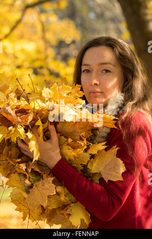 Femme avec les cheveux bruns à la tenue d'une forêt d'automne feuilles d'érable jaune Banque D'Images