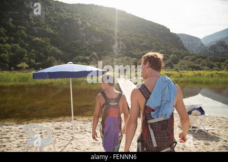 Vue arrière de jeunes hommes portant des sacs à dos sur la plage, Cala Luna, Sardaigne, Italie Banque D'Images