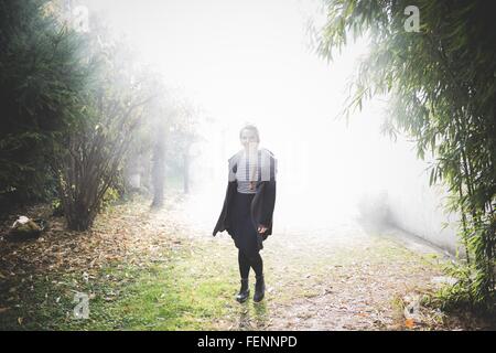 Longueur pleine vue de face of young woman standing in misty garden looking at camera smiling Banque D'Images