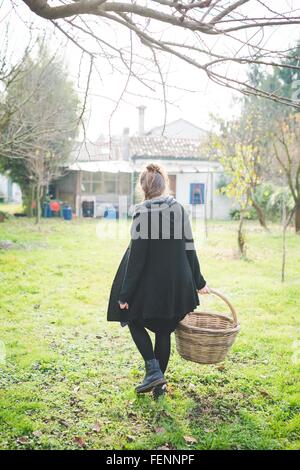 Vue arrière sur toute la longueur de la jeune femme en transportant le jardin panier osier Banque D'Images