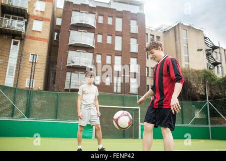 Deux jeunes hommes jouent au football sur un terrain de football urbain Banque D'Images