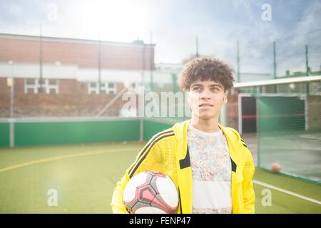 Portrait of young man holding foot, sur un terrain de football urbain Banque D'Images