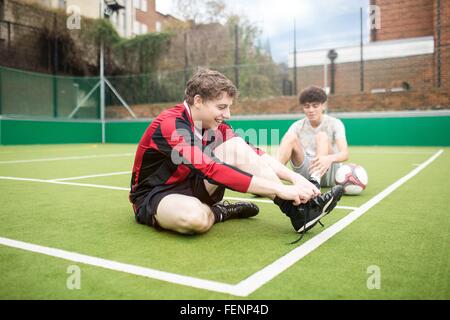Deux jeunes hommes sur un terrain de football urbain, faire ses lacets Banque D'Images