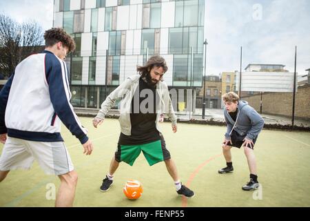 Groupe d'adultes qui jouent au football sur un terrain de football urbain Banque D'Images