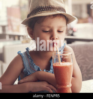 Fun kid girl in hat smoothie potable de verre de jus dans Street Café de la ville. Tonique closeup portrait Banque D'Images