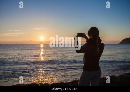 Vue arrière de la silhouette du jeune femme photographiant sunset over sea, Villasimius, Sardaigne, Italie Banque D'Images