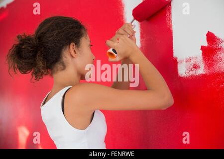 Girl painting wall red with paint roller Banque D'Images