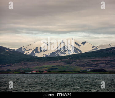 Le nord de l'Islande, Islande. 1er août 2015. Un règlement est situé sur les pentes de l'impressionnant des montagnes enneigées qui plongent dans les eaux d'¶EyjafjÃ rÃ°ur, le plus long fjord de nord de l'Islande. À côté de l'agriculture et de la pêche le tourisme est devenu un secteur en pleine croissance de l'économie et de l'Islande est devenue une destination touristique favorite. © Arnold Drapkin/ZUMA/Alamy Fil Live News Banque D'Images