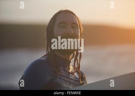 Portrait of young male surfer carrying surfboard, Devon, England, UK Banque D'Images