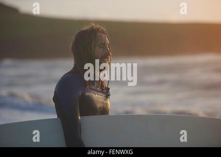 Young male surfer carrying surfboard, Devon, England, UK Banque D'Images