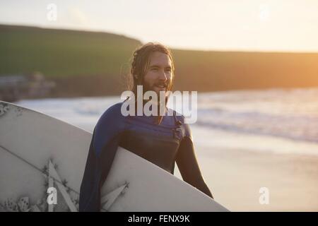 Portrait of young male surfer carrying surfboard on beach, Devon, England, UK Banque D'Images