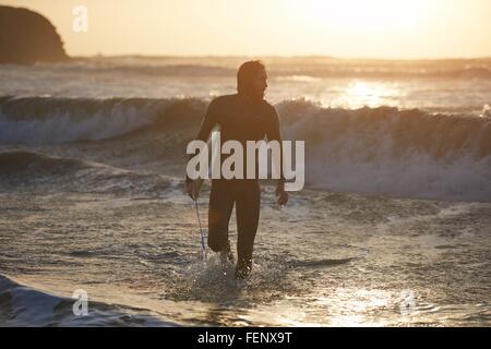 Silhouette de jeune homme surfer carrying surfboard in sea, Devon, England, UK Banque D'Images