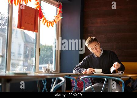 Jeune homme seul dans un café à boire du café et reading magazine Banque D'Images