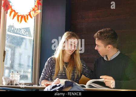 Jeune couple sur date dans cafe reading magazine Banque D'Images