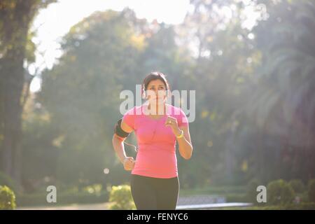 Vue avant du young woman wearing headphones et brassard jogging in park Banque D'Images