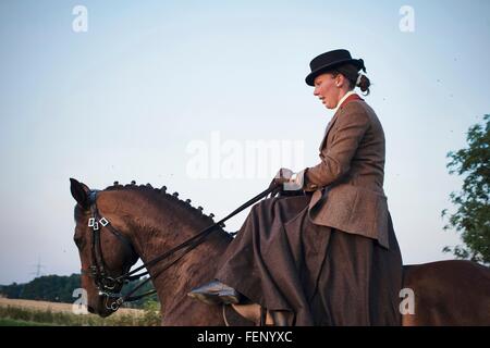 Mid adult woman riding et de formation dans le champ cheval de dressage Banque D'Images