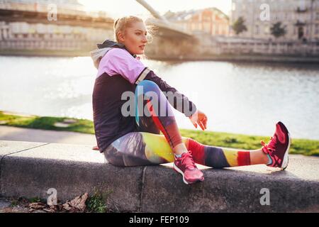 Mid adult female runner faire réchauffer l'exercice sur mur riverside Banque D'Images