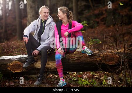 Sur toute la longueur du vêtement de sport couple assis sur un arbre tombé, smiling Banque D'Images