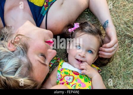 Overhead portrait of mid adult woman and blue eyed toddler daughter lying on grass Banque D'Images