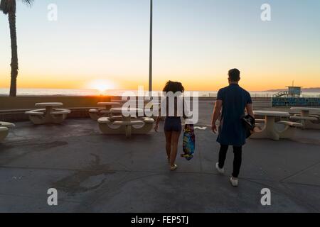 Couple en train de marcher près de la plage, holding skateboards, vue arrière Banque D'Images