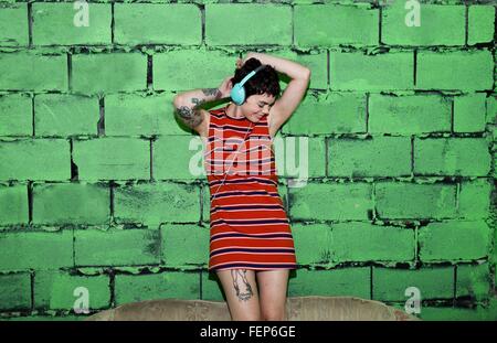 Mid adult woman with tattoos, portant des écouteurs, la danse Banque D'Images