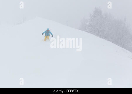 Un skieur est le ski en un temps brumeux. Il prend une pente enneigée à partir de la descente dans la montagne. Banque D'Images