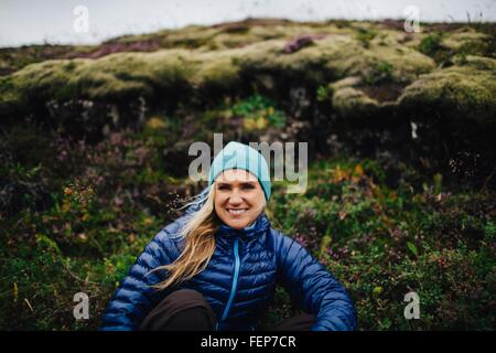 Vue avant du Mid adult woman s'accroupit en face de mound wearing Knit hat smiling at camera, Islande Banque D'Images