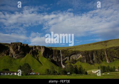 Village isolé par une chute d'eau coulant sur une chaîne de montagnes, l'Islande Banque D'Images