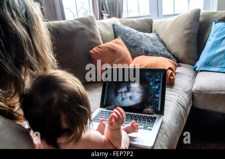 Plus d'épaule de la mère sur le canapé en regardant des photos de fille on laptop Banque D'Images