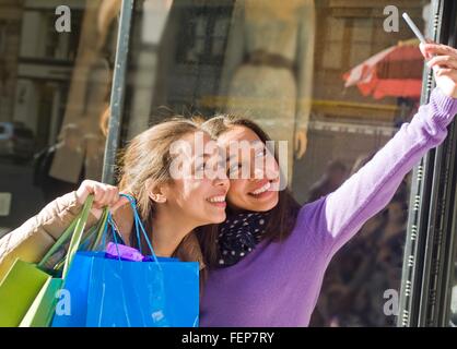 Les jeunes adultes de sexe féminin des jumeaux en ville prendre sur smartphone selfies with shopping bags Banque D'Images