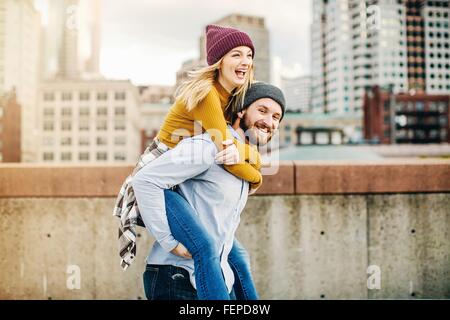 Young man giving girlfriend piggyback sur un toit-terrasse de la ville Banque D'Images