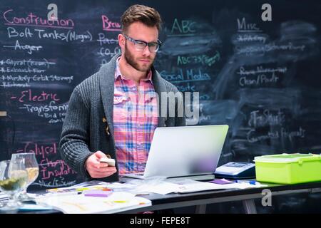 Jeune homme dans le lieu de travail à l'aide d'ordinateur portable holding smartphone Banque D'Images