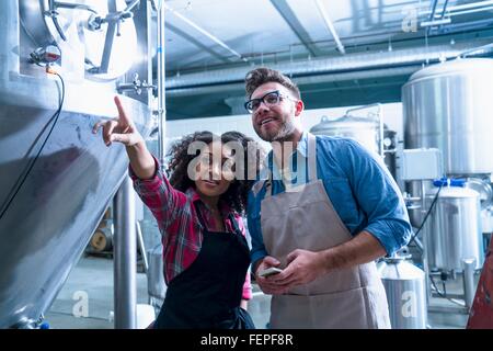 Collègues de brasserie par fermentation réservoir conique, pointant à up smiling Banque D'Images