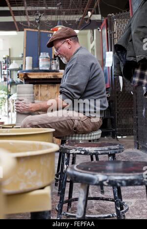 Vue de côté de potter en séance de l'atelier de poterie au façonnement de roue pot en argile Banque D'Images