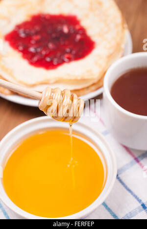 Dégoulinant de miel une cuillère de crêpes et de thé sur la table de cuisine. Banque D'Images