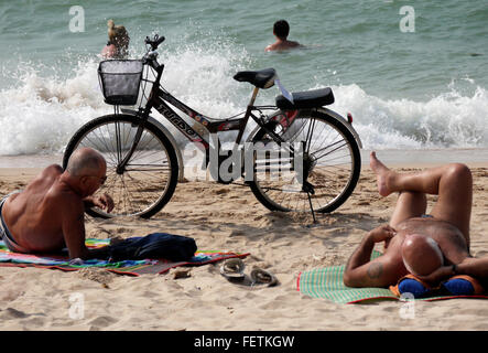 Un vélo avec un siège passager leurs garé sur la plage à Pattaya en Thaïlande avec deux hommes âgés bronzer et se détendre Banque D'Images