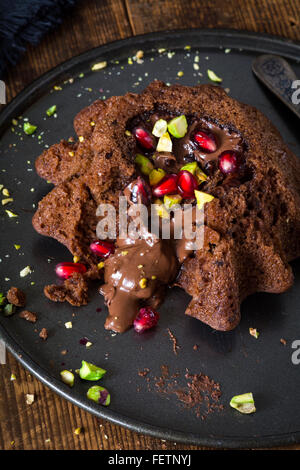 La lave de chocolat gâteau décoré avec les pistaches hachées et de graines de grenade. Tasse de café noir de côté. Fond de bois rustique
