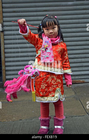 Une belle fille chinoise de 5 ans dans une robe et un petit dragon à la parade du Nouvel An lunaire. Mott Street à Chinatown, NYC Banque D'Images