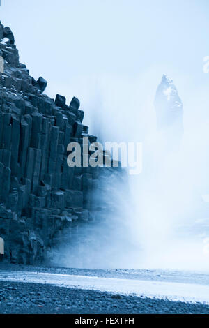 Vagues éclaboussant contre les rochers de roches basaltes Reynisdrangar à la plage de sable noir Reynisfjara, en Islande du Sud en janvier - longue exposition Banque D'Images