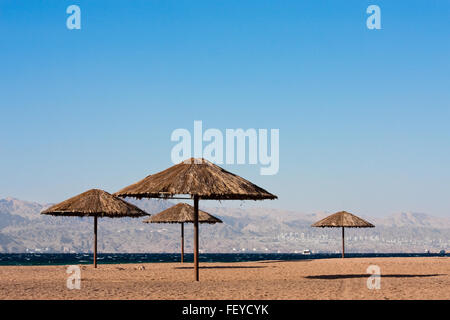 Près de parasols sur la plage de la mer lire à Aqaba, Jordanie. Ville d'Eilat, l'Égypte en arrière-plan. Banque D'Images