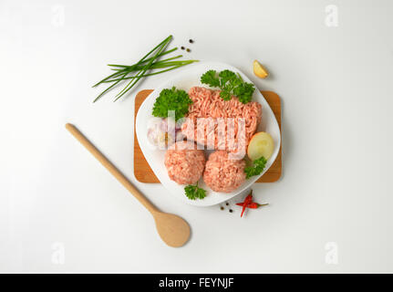 Assiette de boulettes de viande crue et de condiments sur planche à découper en bois Banque D'Images