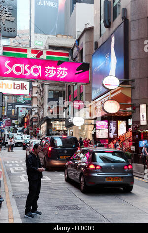 La lecture de l'homme son téléphone portable traverser une rue passante proche du niveau de l'île de Hong Kong, Hong Kong SAR, Chine Banque D'Images