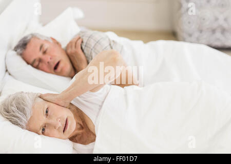 Awake senior woman in bed couvrant ses oreilles Banque D'Images