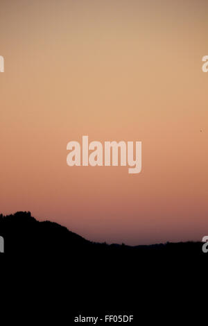 Un ciel clair au coucher du soleil avec des tons rose, orange et marron et silhouetté hills et d'arbres. Banque D'Images